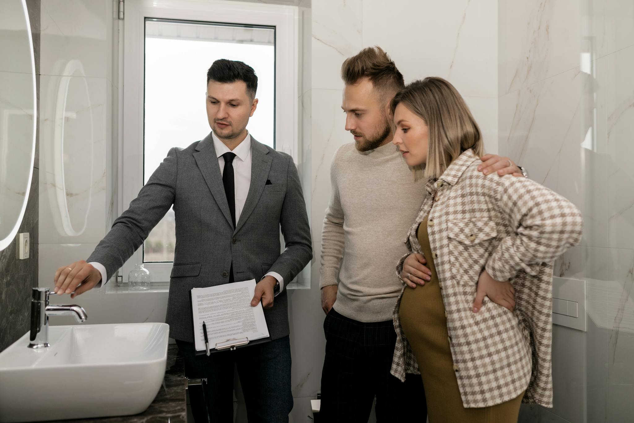 Real estate agent demonstrates bathroom features to a young couple during a house tour.