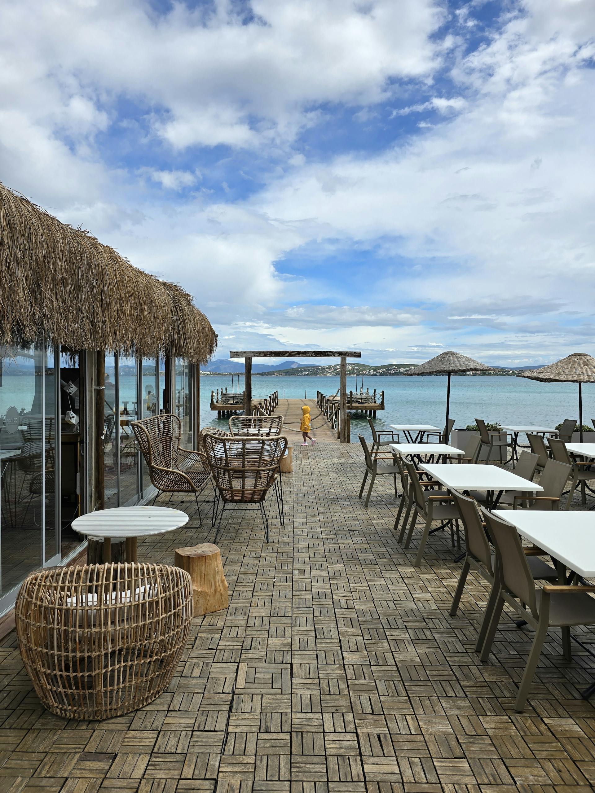 Serene beachfront cafe with straw umbrellas and ocean view under a cloudy sky. Perfect for vacation vibes.